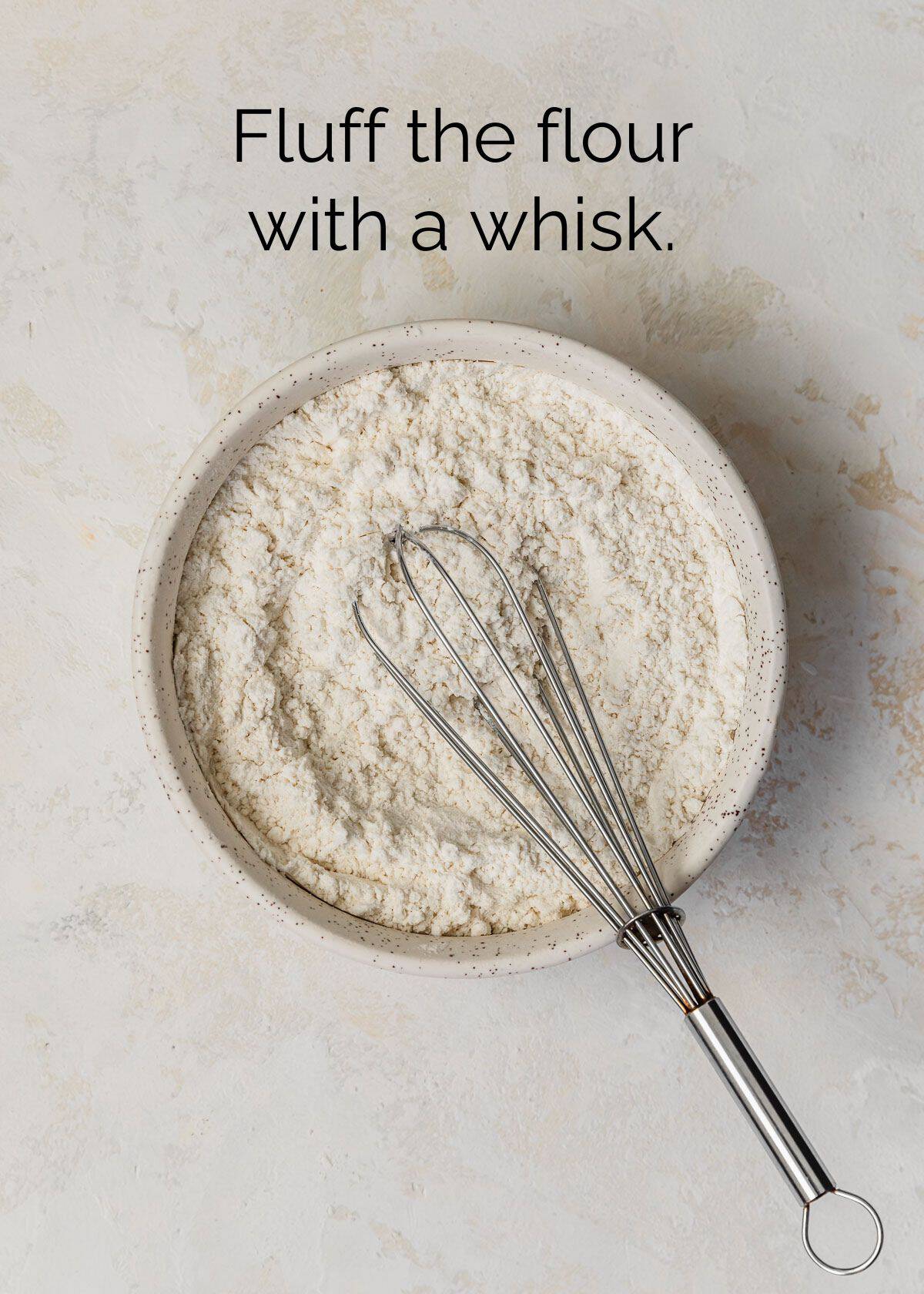 How to measure ingredients for small batch baking with measuring cups. A white bowl of flour with a whisk on a tan counter.