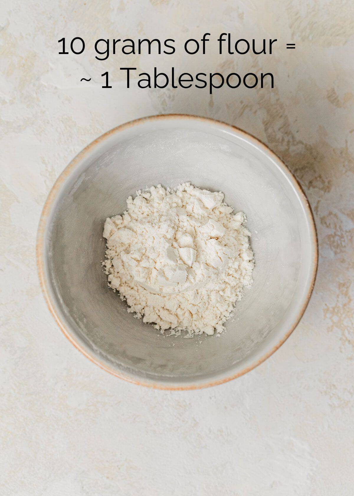 How to measure ingredients for small batch baking. A white bowl of flour on a tan counter.