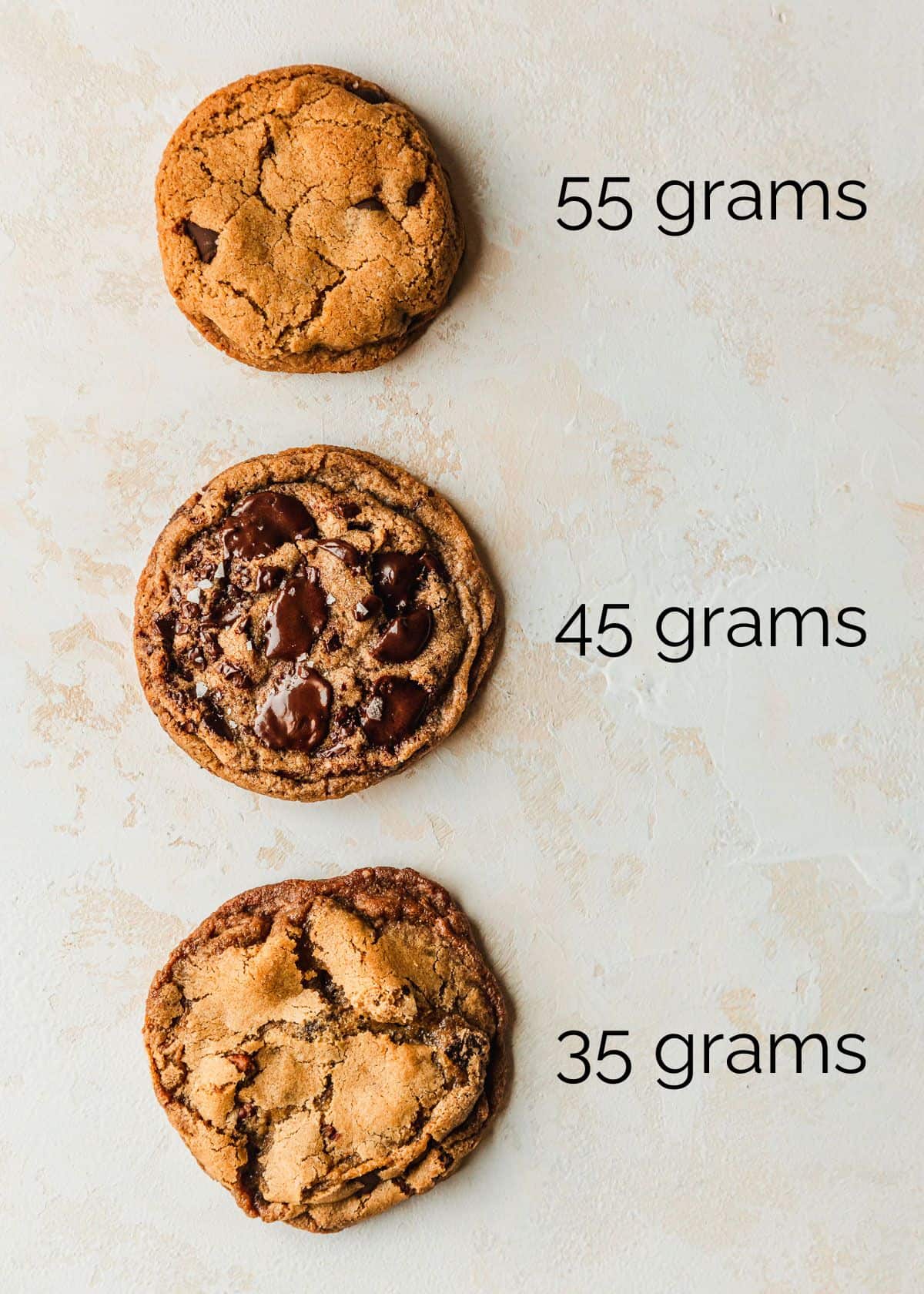 Three chocolate chip cookies on a tan counter.