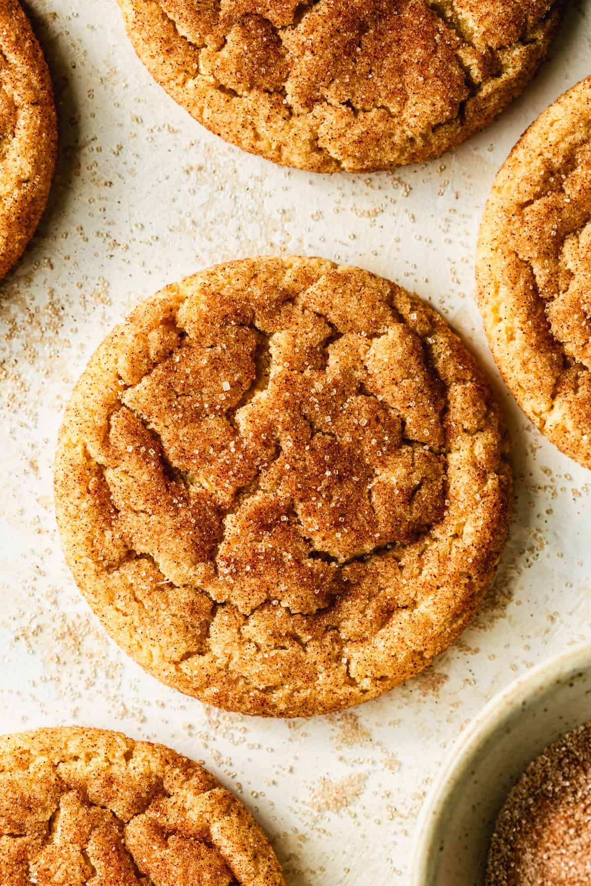 Rows of small batch snickerdoodles on a tan table next to a white bowl of cinnamon sugar.