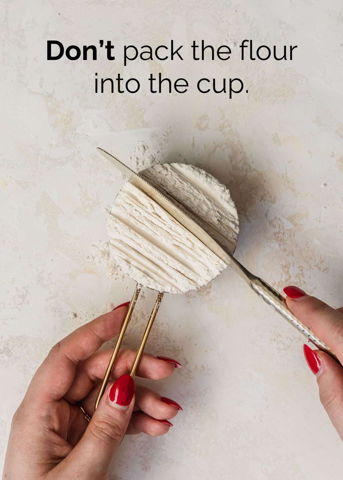 How to measure flour for small batch baking. A hand using a knife to pack flour into a gold measuring cup.