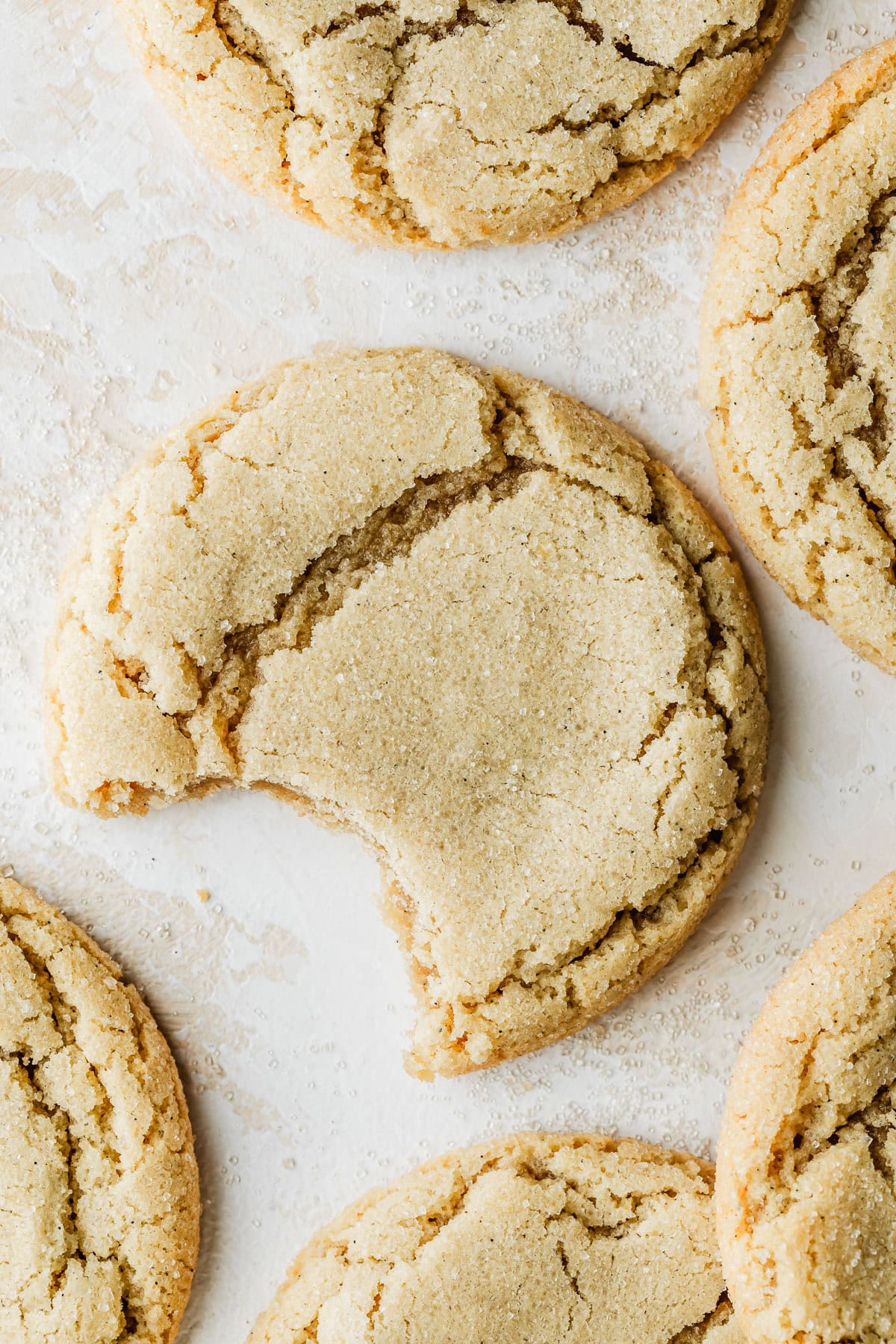 A cookie with a bite taken out of it next to rows of small batch sugar cookies on a white and beige counter.