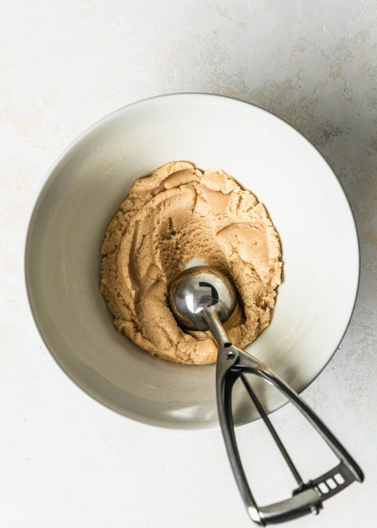 A white bowl of small batch sugar cookies dough with a scoop on a white table.