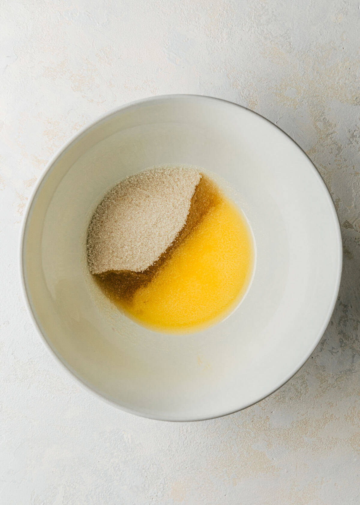 A white bowl of melted butter and sugar on a white counter.