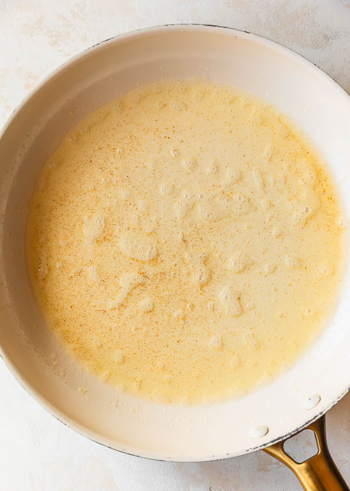 A white pan of brown butter on a tan counter.