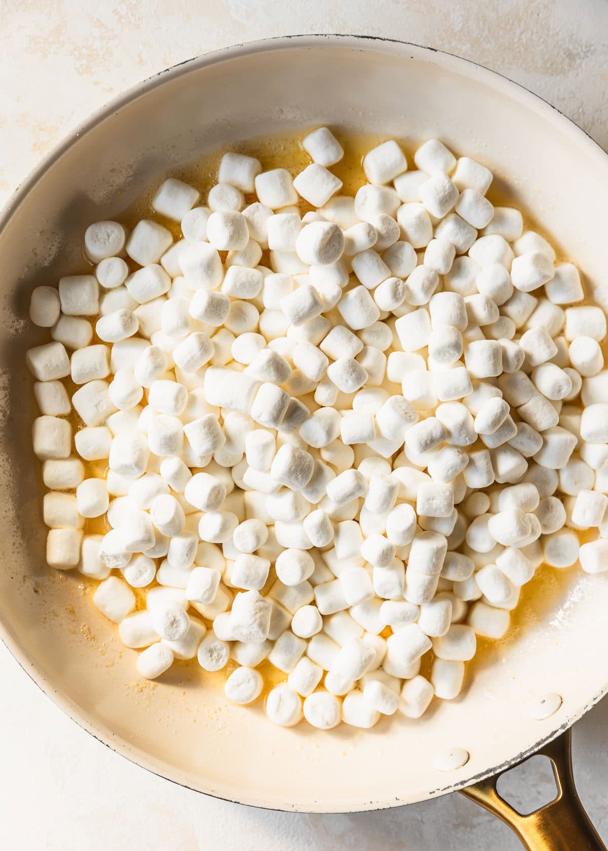 A white pan of brown butter and marshmallows on a tan backdrop.