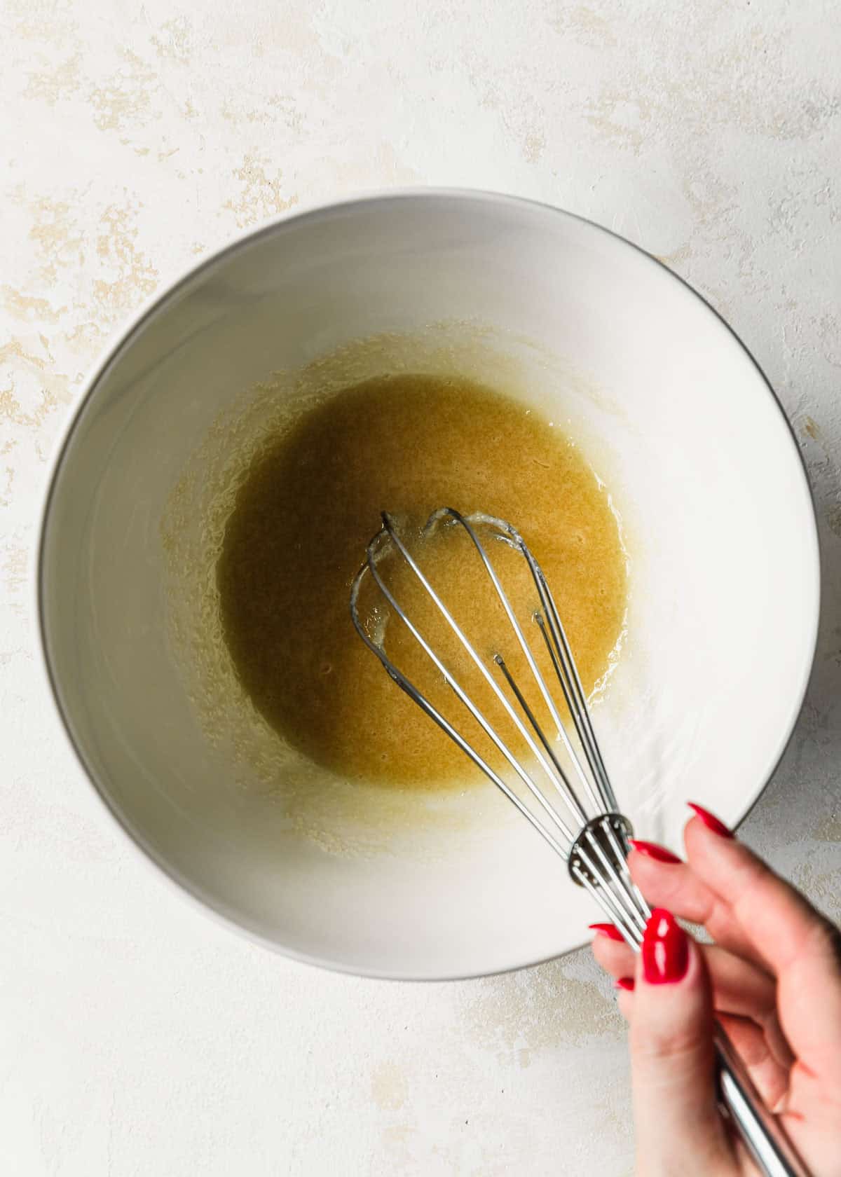 A hand whisking butter and sugar in a white bowl.