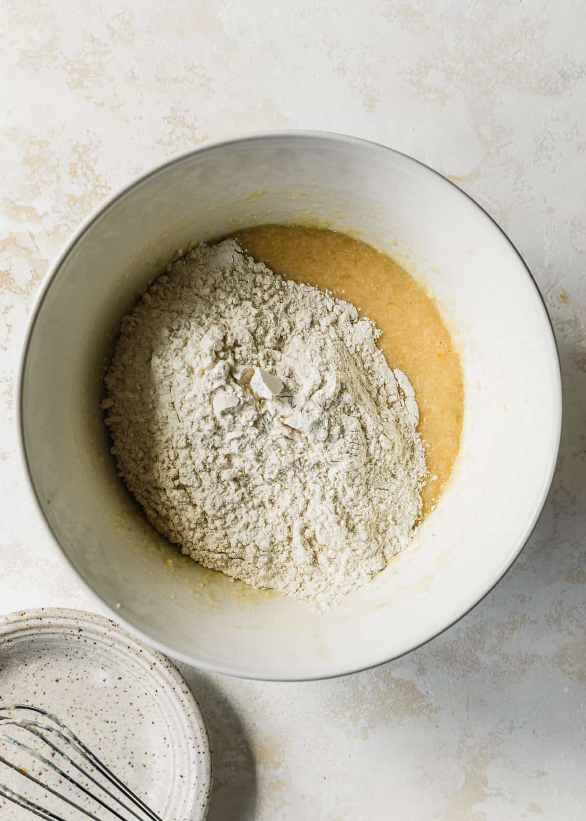 A white bowl of mixed butter, sugar, eggs, buttermilk, and vanilla with flour, baking powder, and salt.