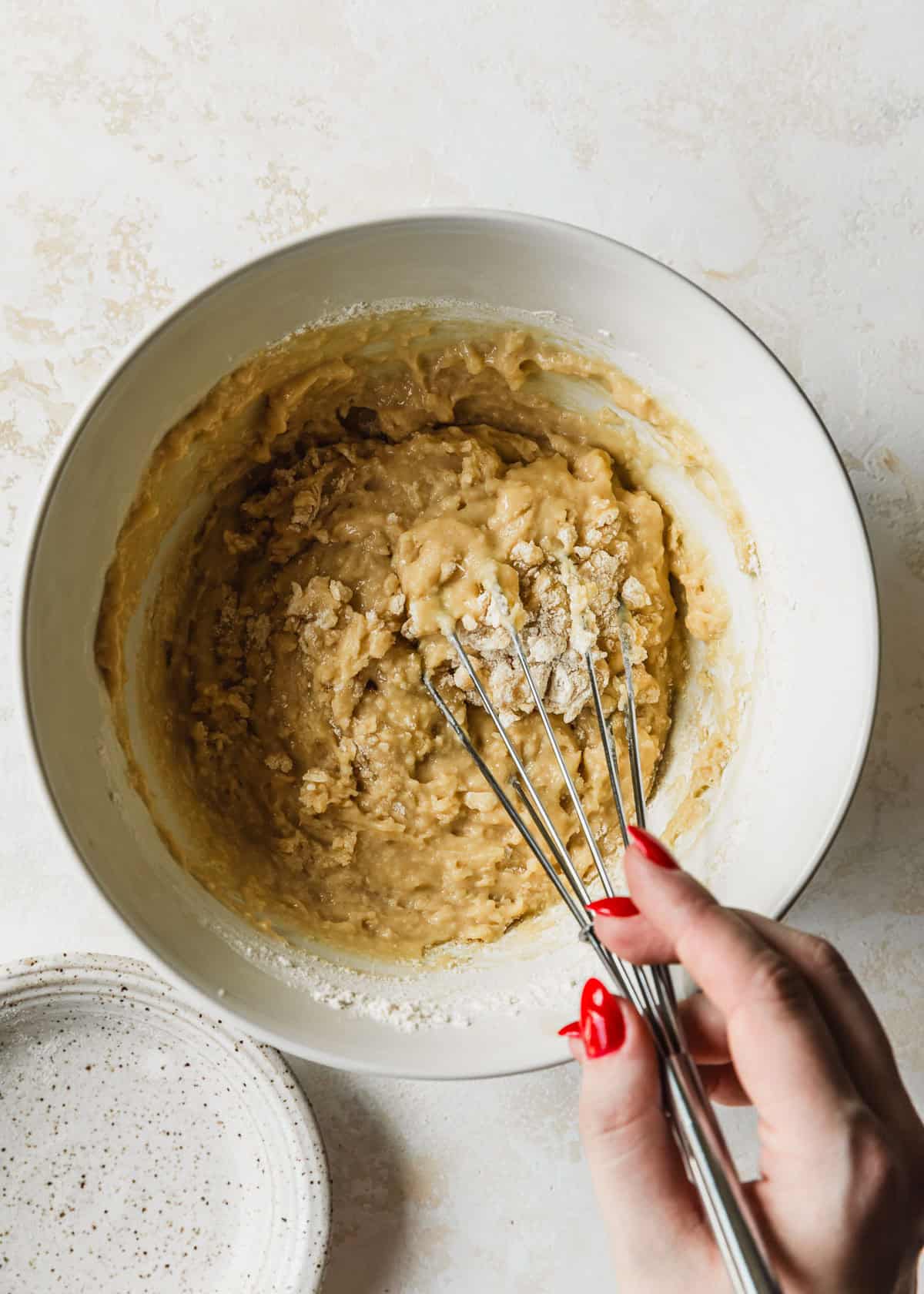 A hand whisking batter for small batch blueberry muffins in a white bowl.