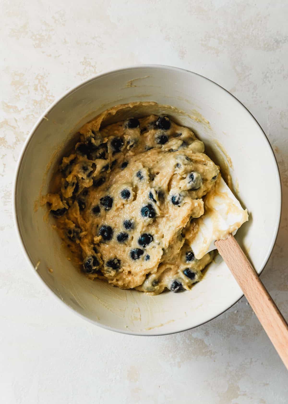 A white bowl of batter for small batch blueberry muffins on a beige counter.