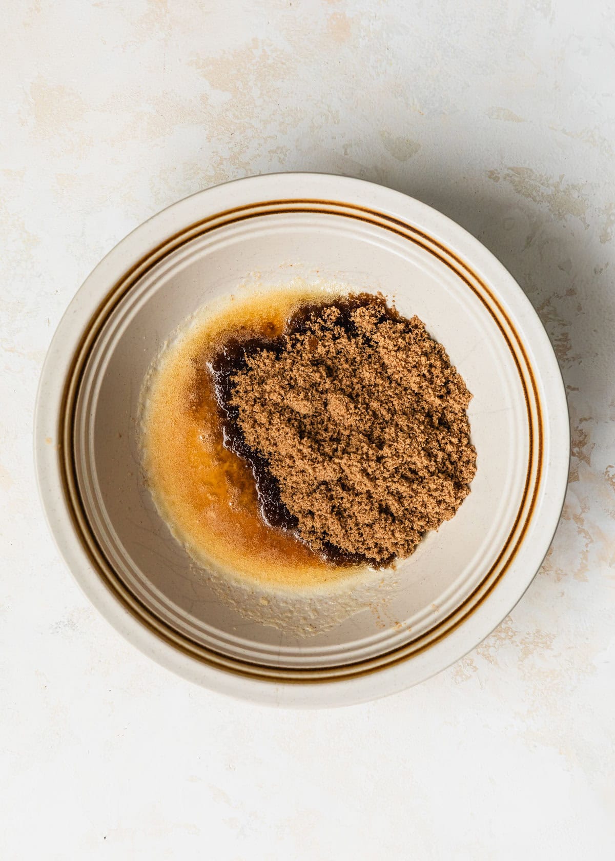 A white bowl of brown butter and brown sugar on a tan counter.
