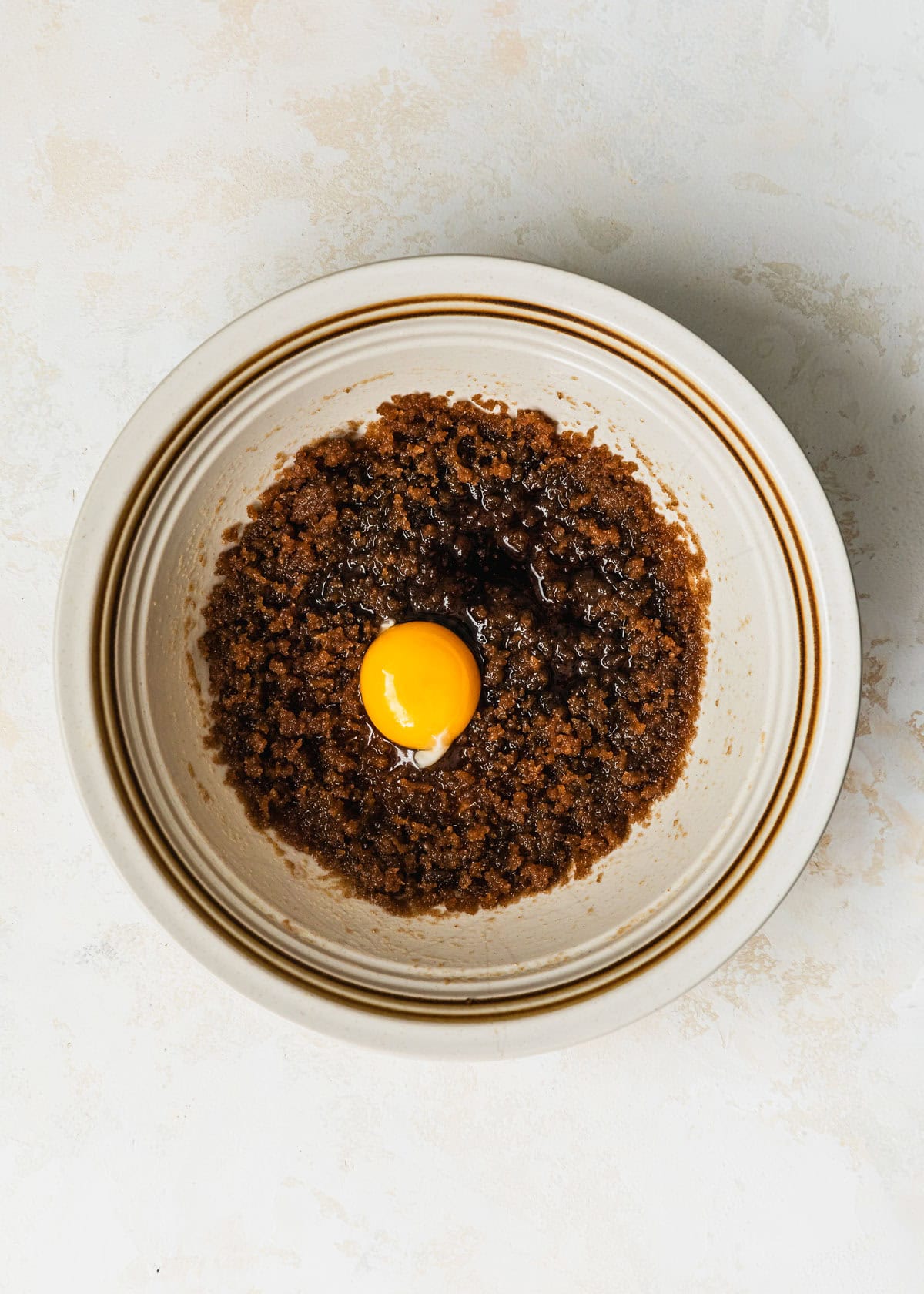 A white bowl of brown butter, brown sugar, and an egg yolk on a tan counter.