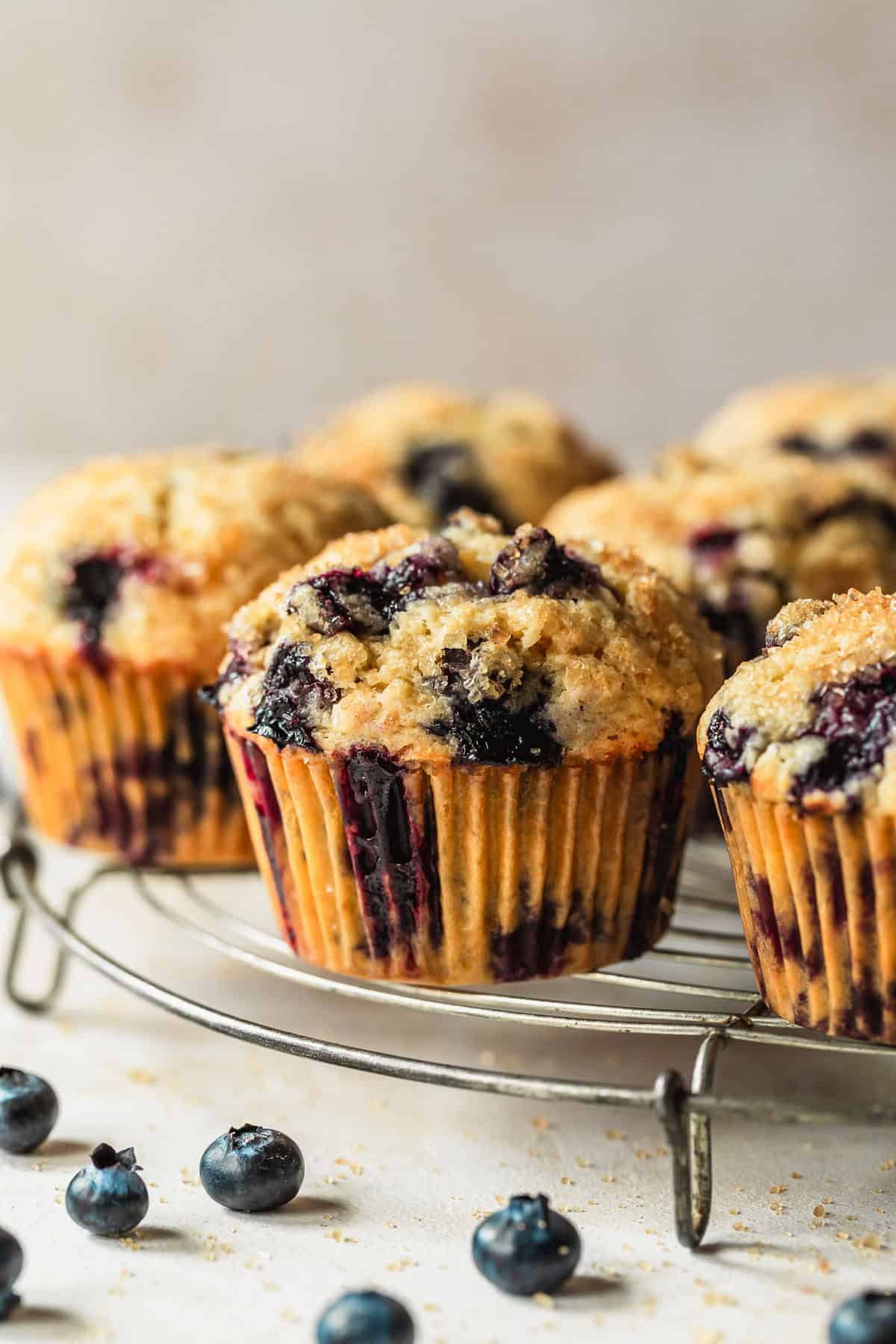 A wire rack of small batch blueberry muffins next to blueberries on a tan counter.