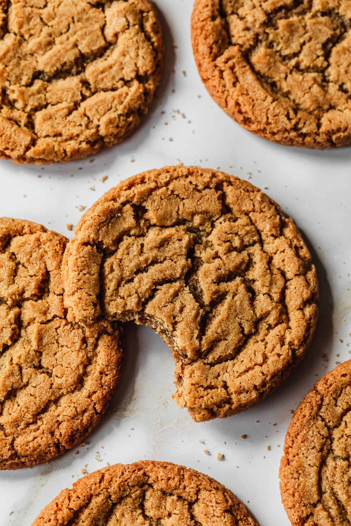 A cookie with a bite taken out of it next to rows of small batch chocolate chipless cookies on a white counter.
