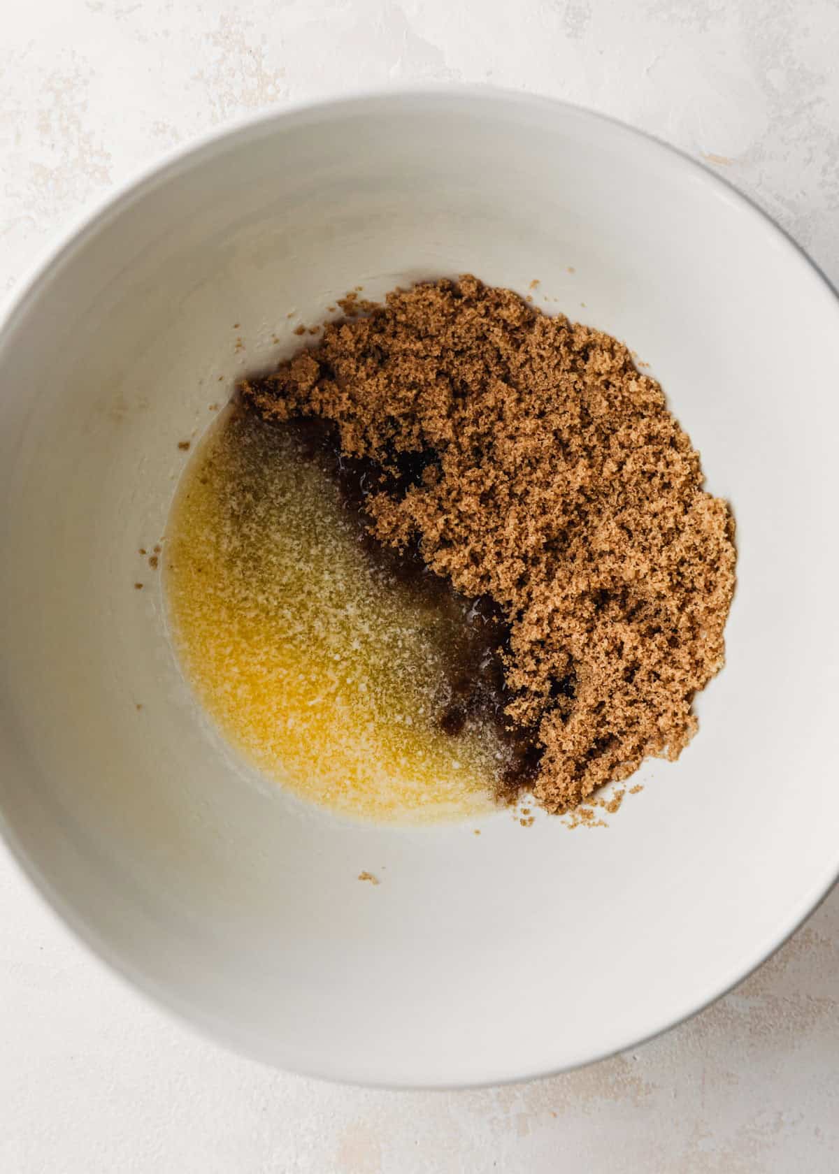 A white bowl of melted butter and brown sugar on a tan counter.