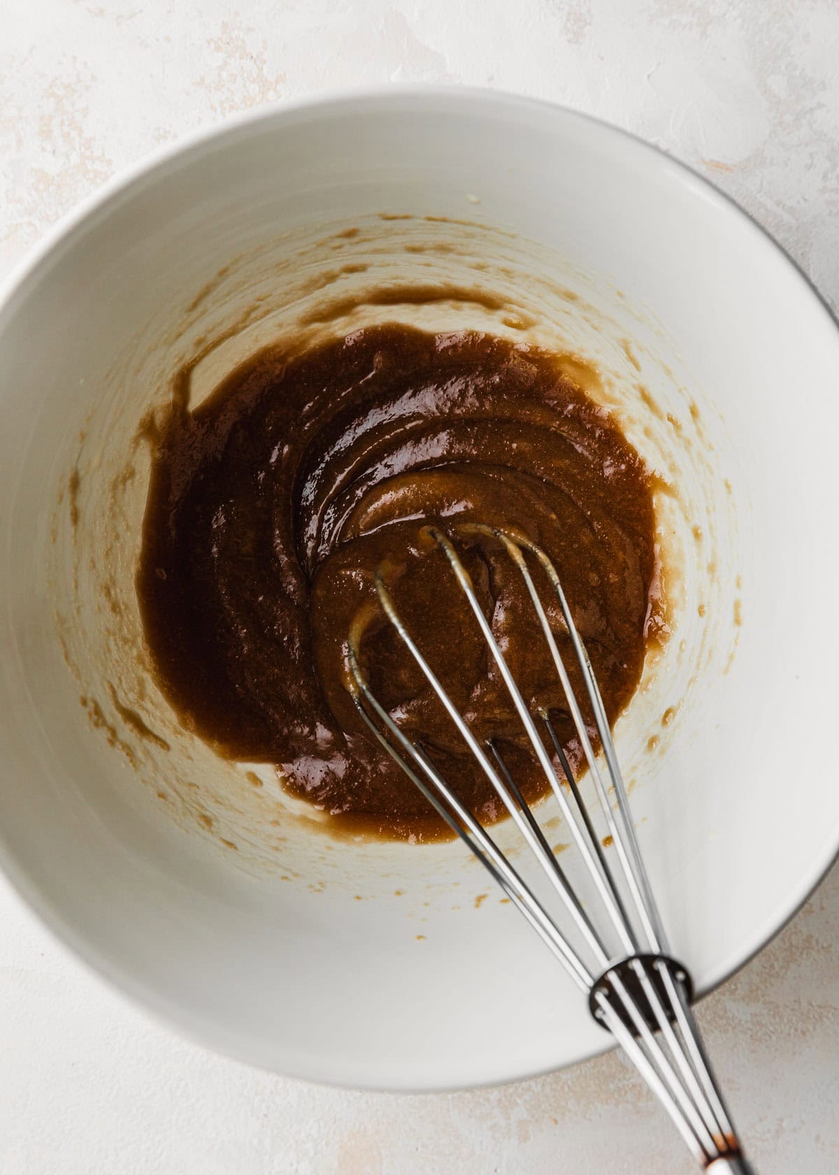 A whisk stirring butter and brown sugar in a white bowl.