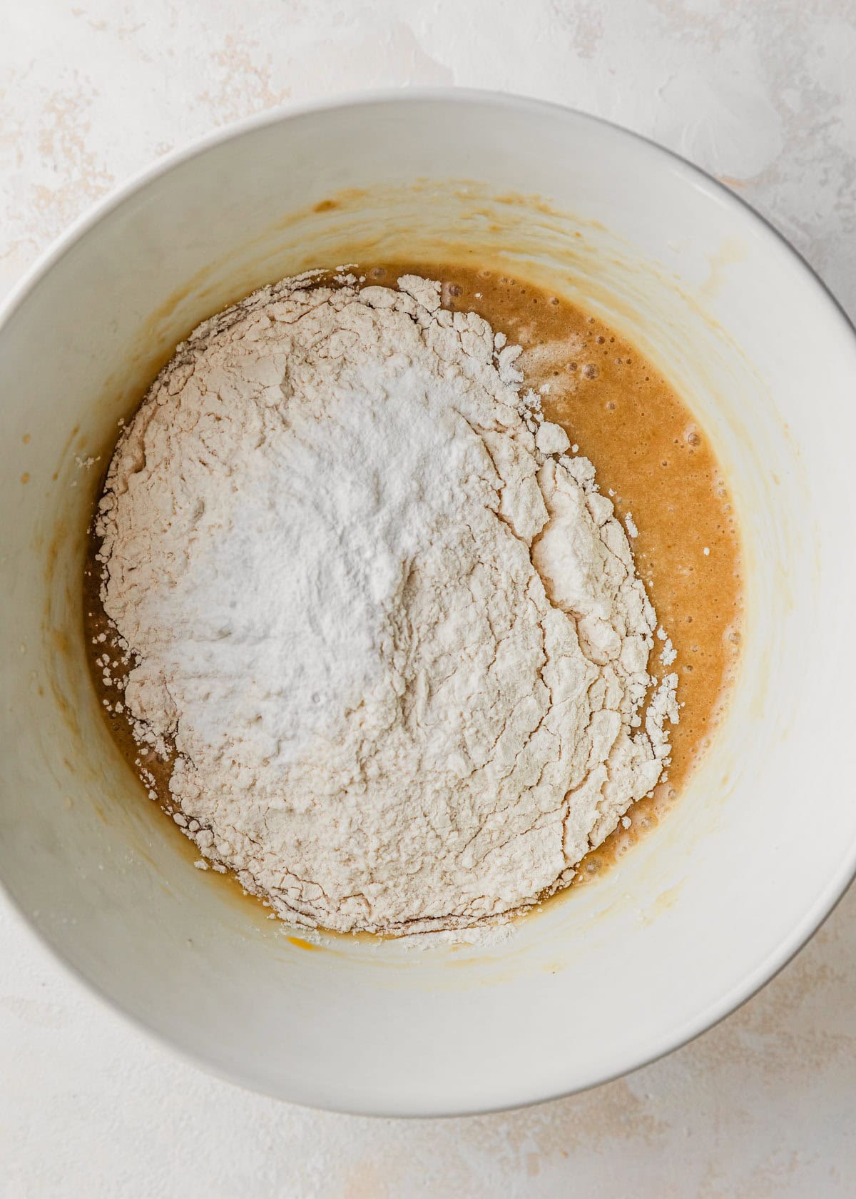 A white bowl of butter, sugar, eggs, and flour on a tan counter.