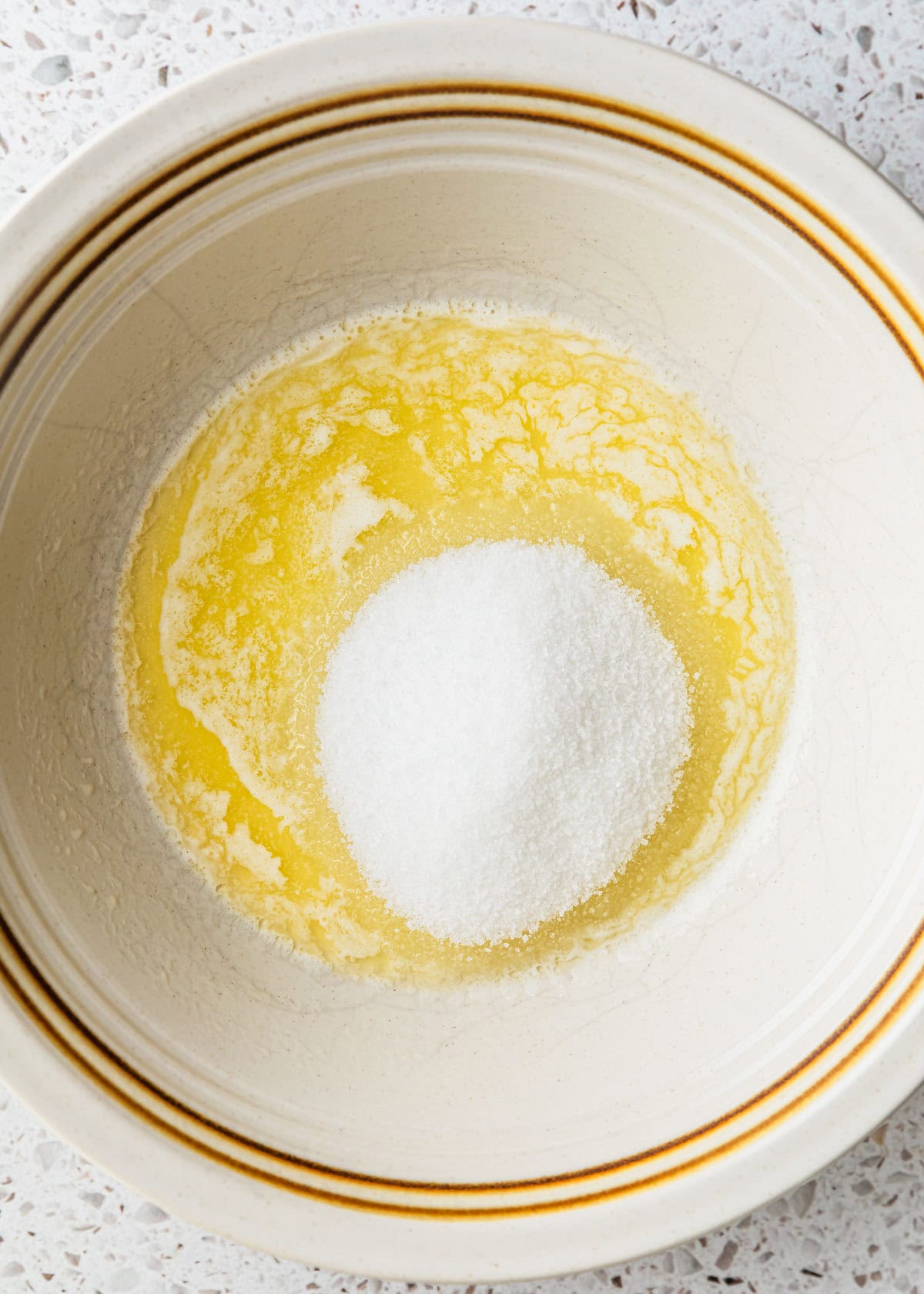 A white bowl of melted butter and sugar on a white terrazzo counter.