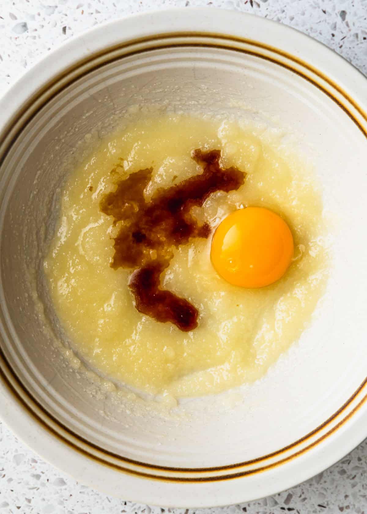 A white bowl of butter, sugar, an egg yolk, and artificial vanilla.