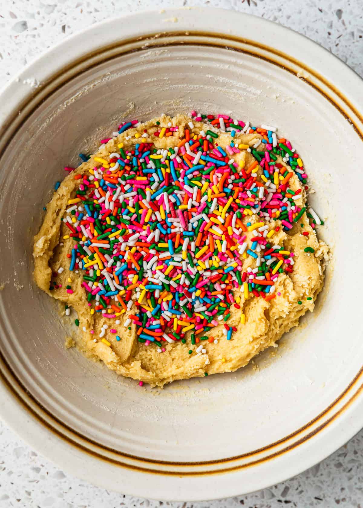 A white bowl of cookie dough with rainbow sprinkles.