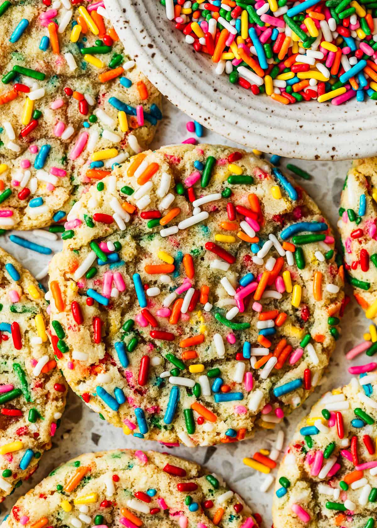 Stacks of small batch funfetti cookies next to a white bowl of rainbow sprinkles.