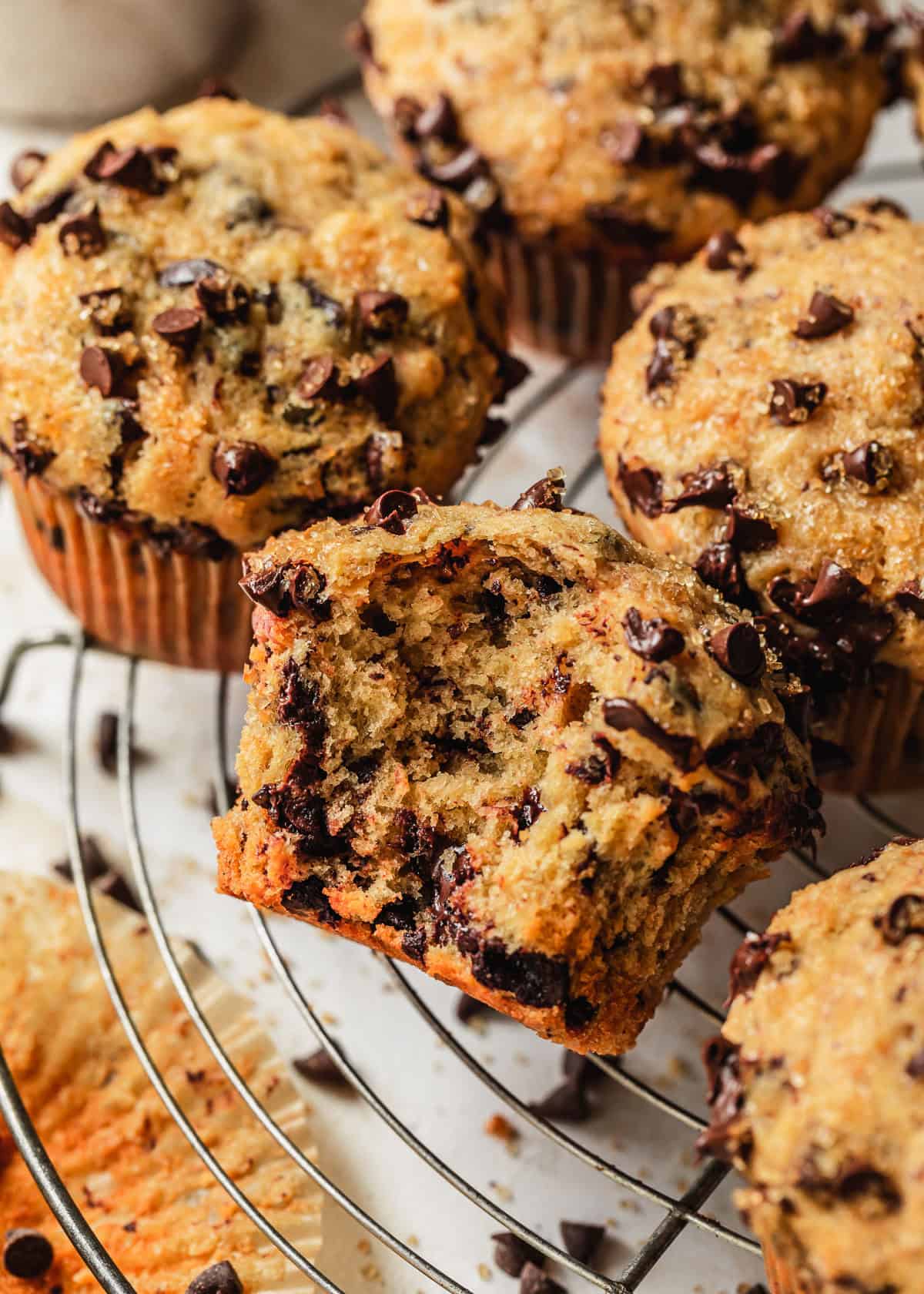 A wire rack of small batch chocolate chip muffins on a white counter covered in raw sugar and chocolate chips.