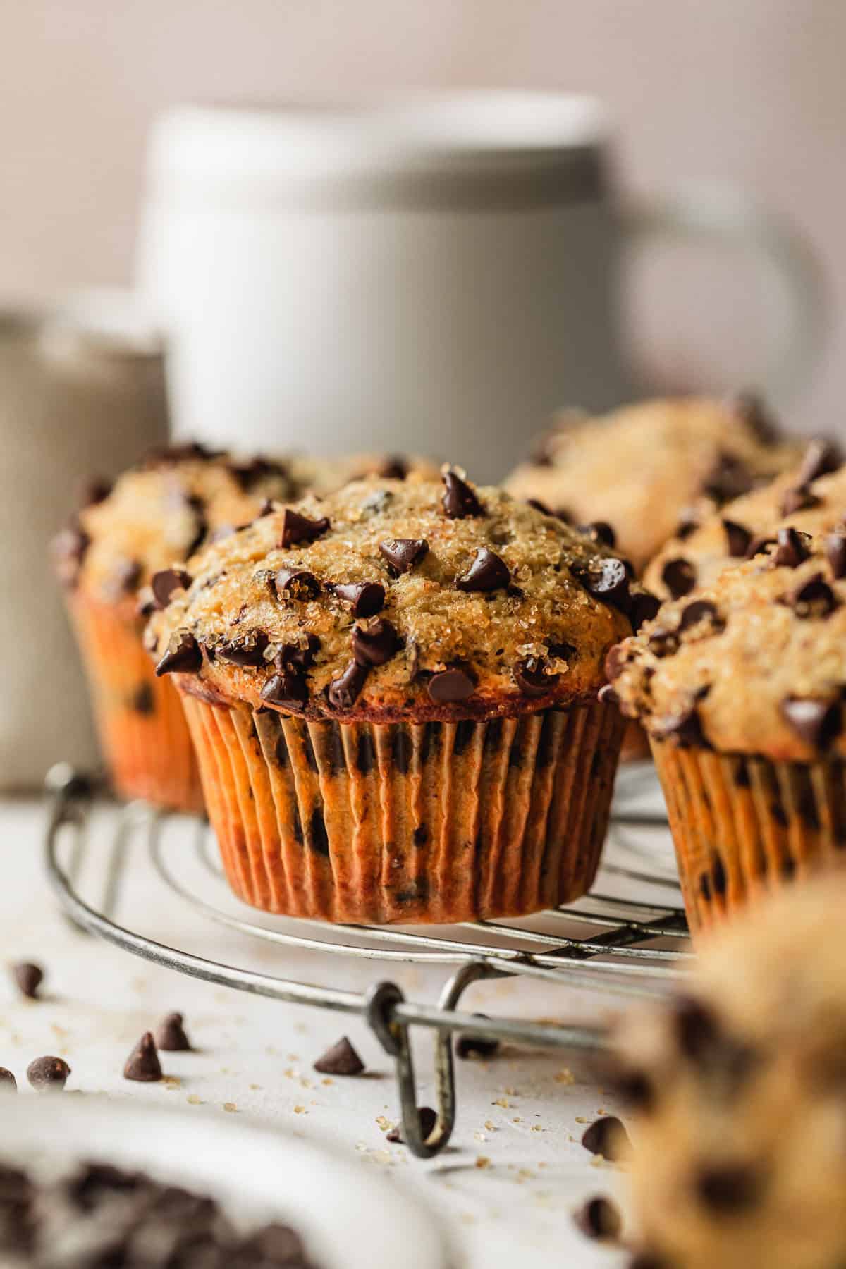 A wire rack of small batch chocolate chip muffins on a tan counter next to a white mug.