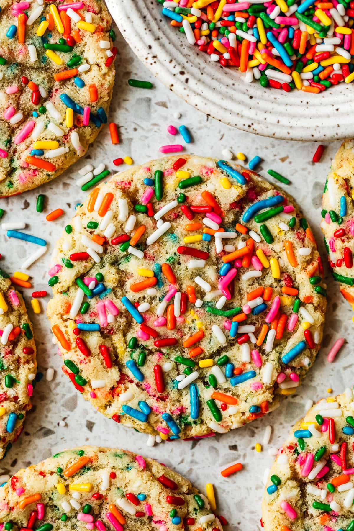 Rows of small batch funfetti cookies on a white terrazzo counter next to a white bowl of rainbow sprinkles.