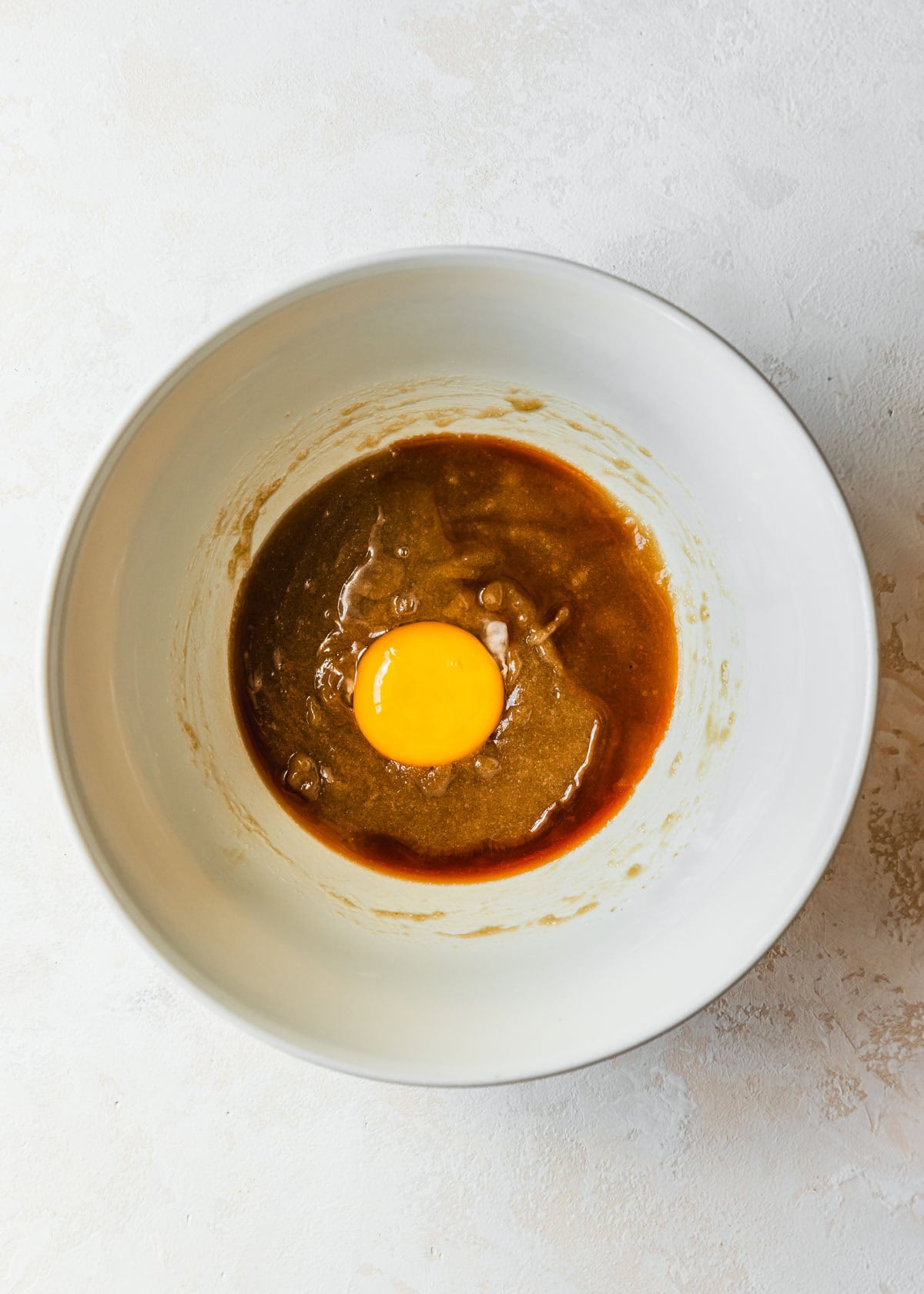 A white bowl of butter, sugar, and an egg yolk on a white counter.