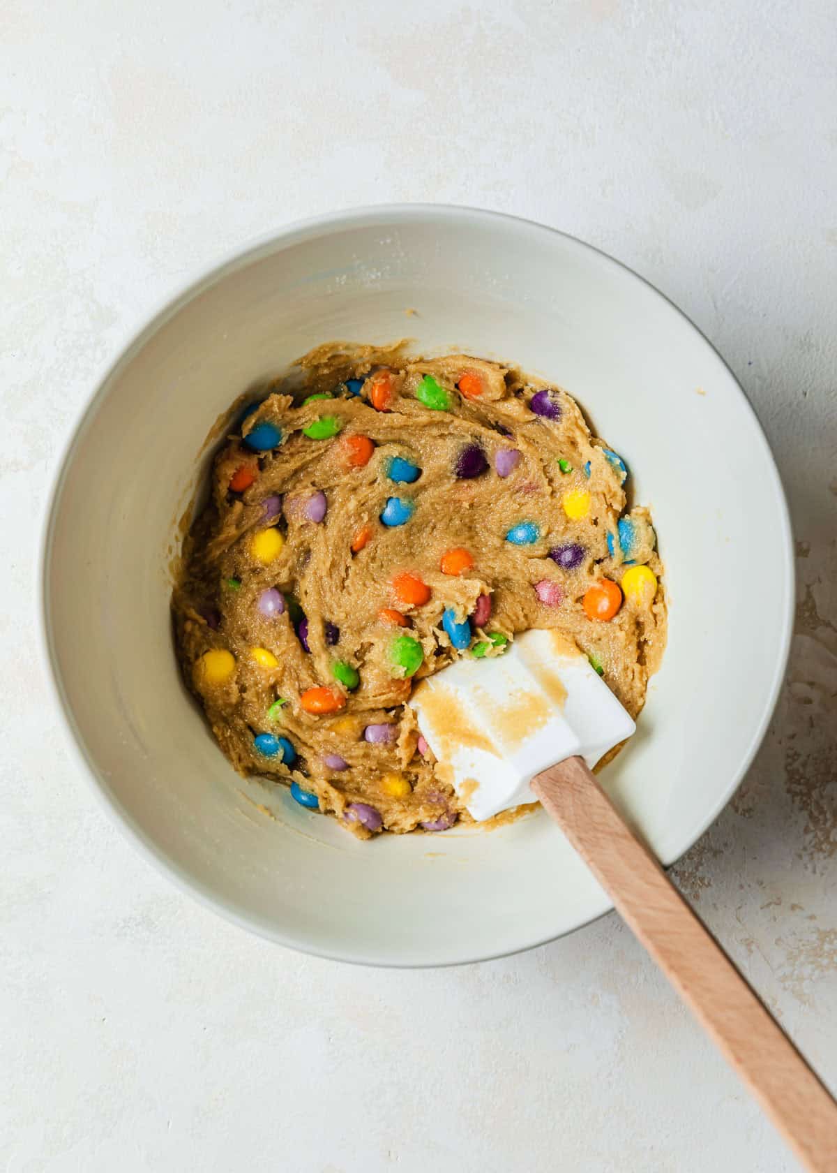 A white bowl of dough for small batch M&M cookies on a tan counter.
