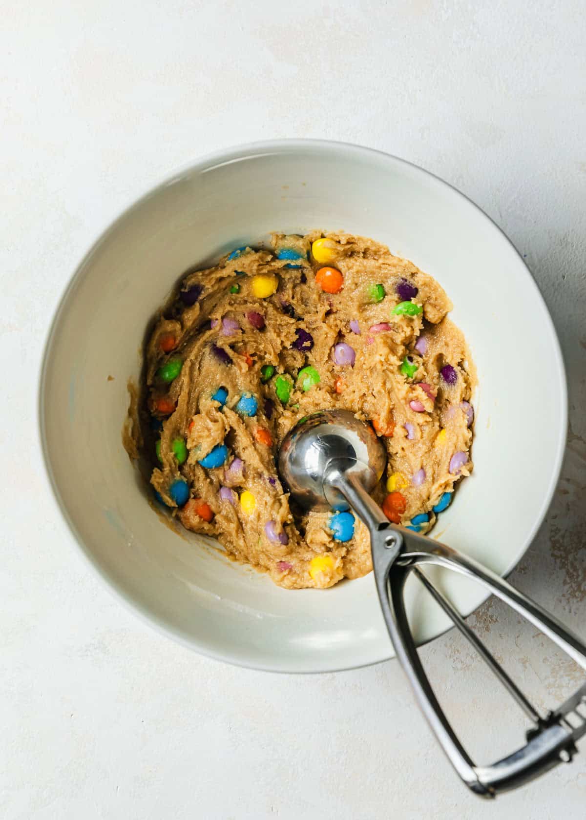 A scoop dividing dough for small batch M&M cookies in a white bowl.