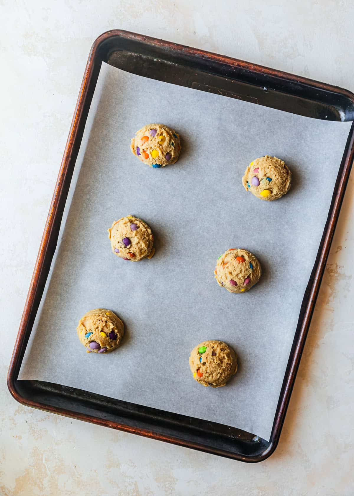 A sheet pan of small batch M&M cookies on a tan counter.