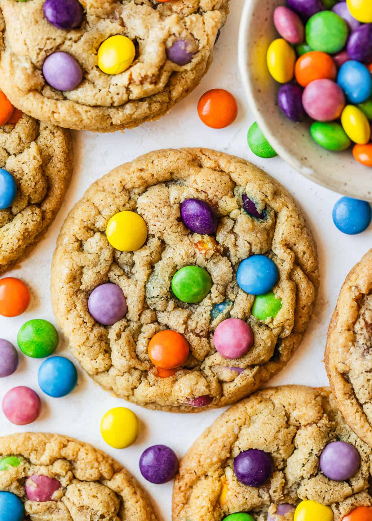 Rows of small batch M&M cookies and a white bowl of M&Ms on a tan counter.