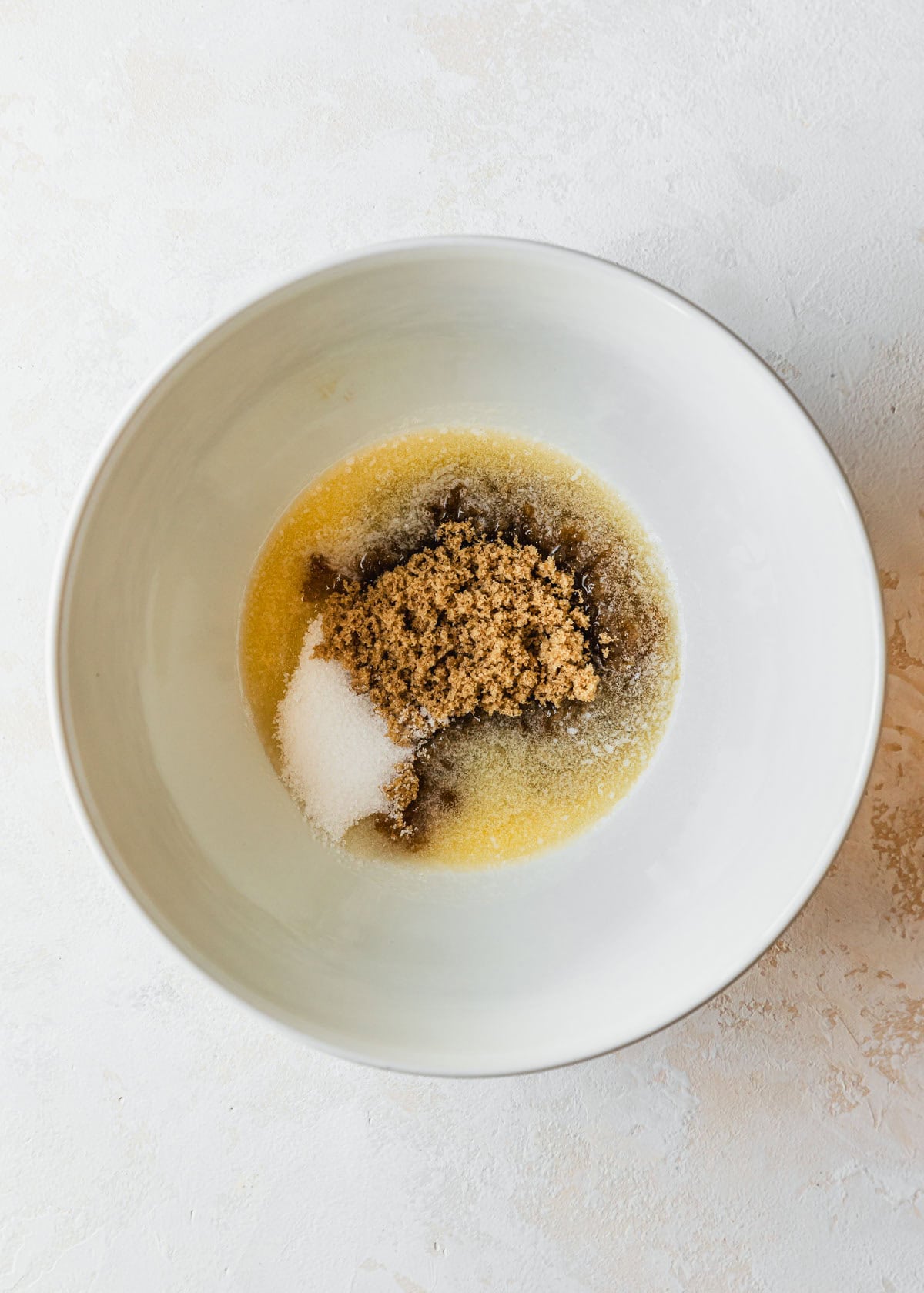A white bowl of butter, brown sugar, and white sugar on a tan counter.