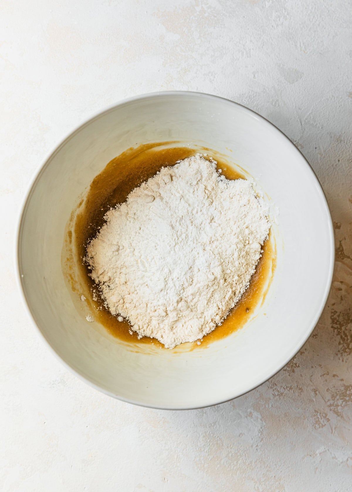 A white bowl of butter, sugars, and flour on a tan counter.
