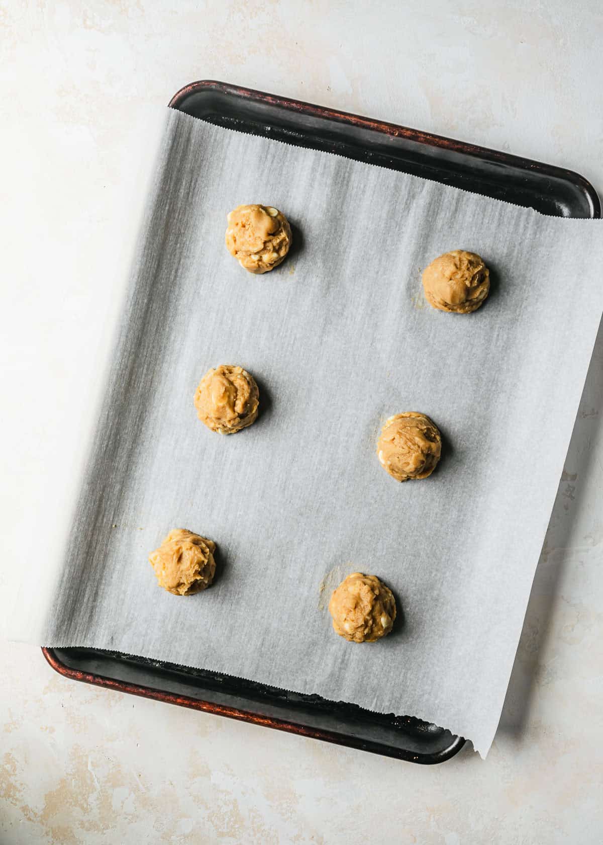 A sheet pan with raw small batch white chocolate macadamia nut cookies on a beige counter.