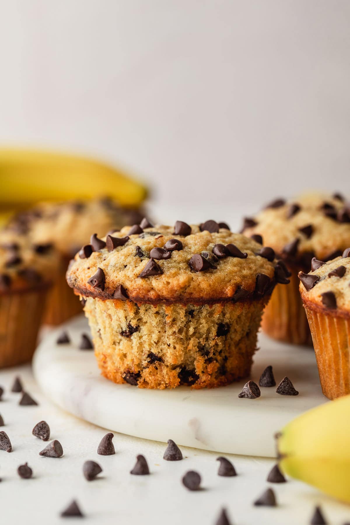Rows of small batch chocolate chip banana muffins on a white marble board next to bananas with a white background.