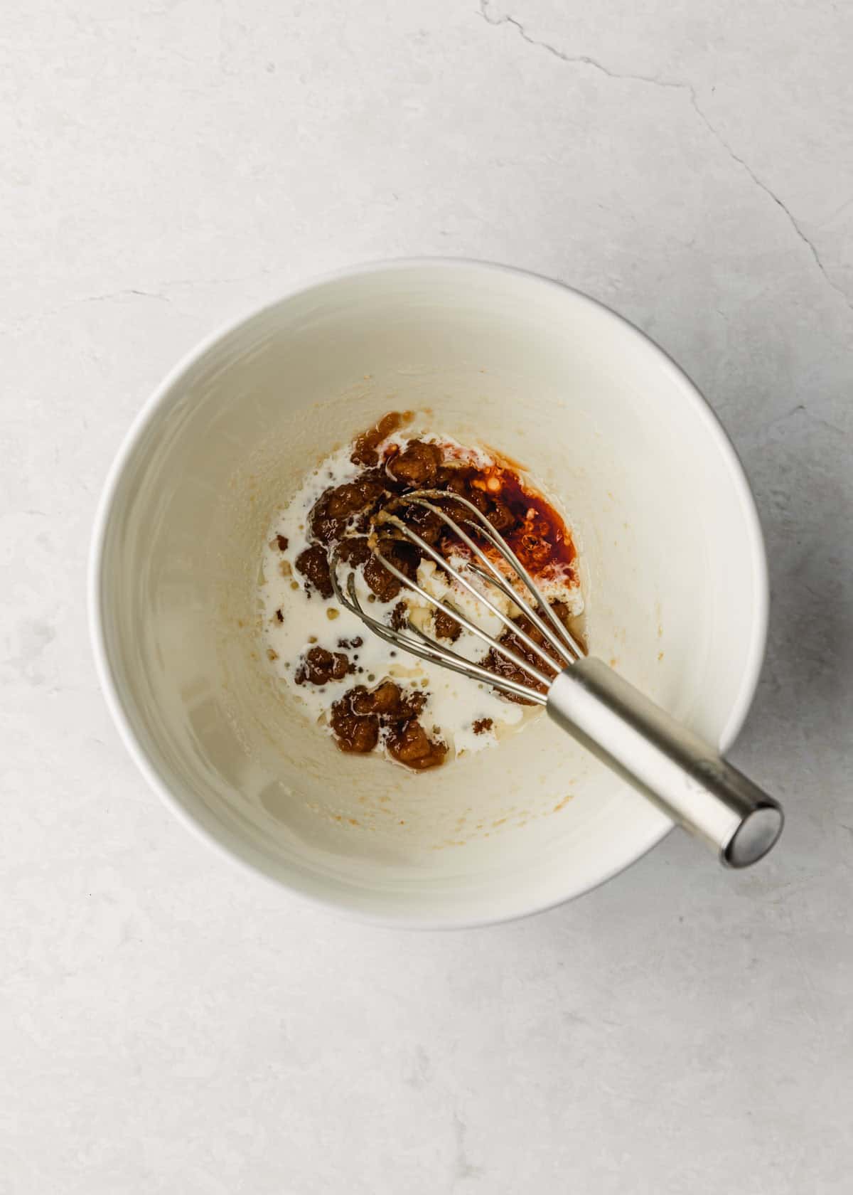 A white bowl of butter, sugar, and heavy cream on a white counter.