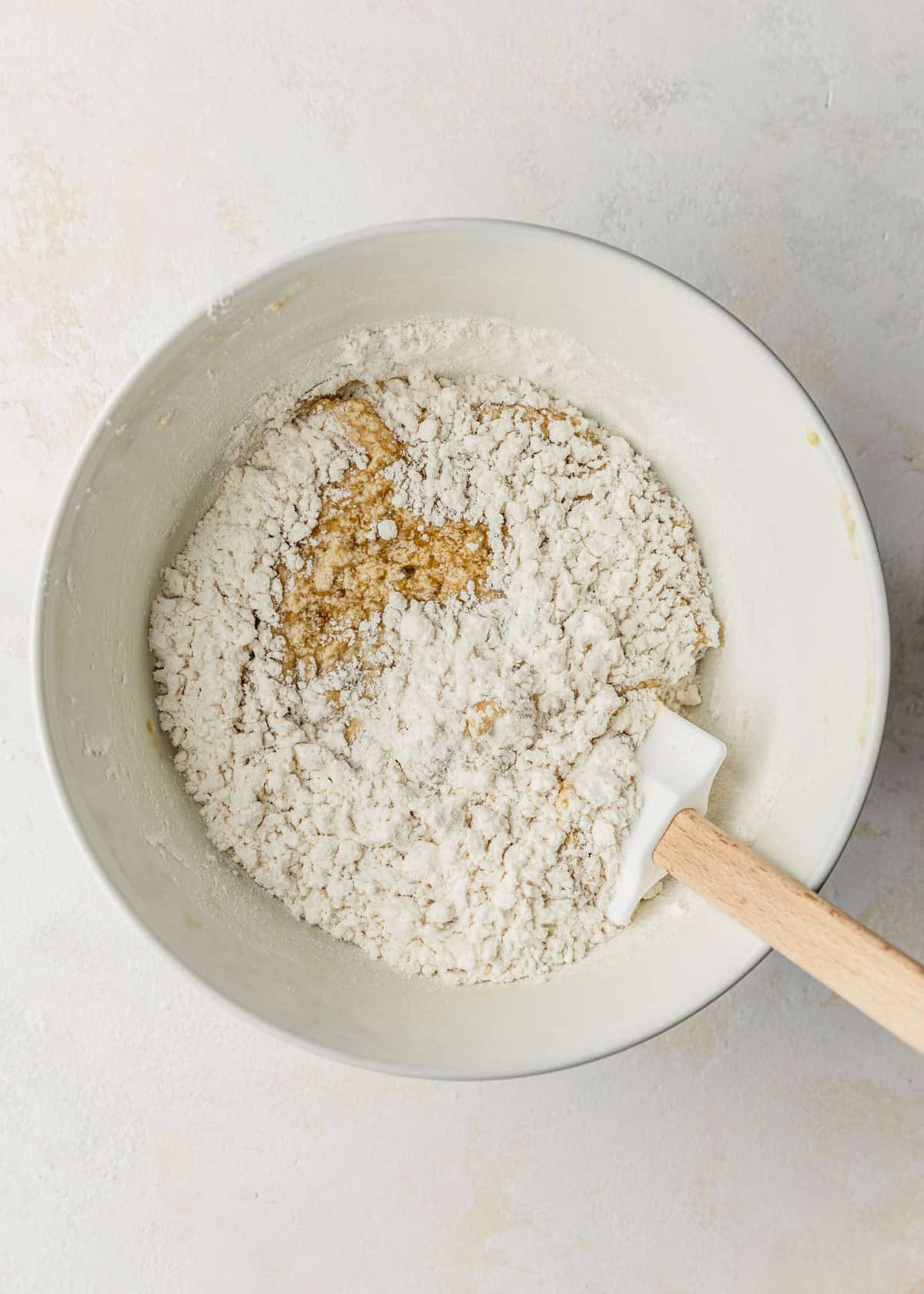 A white bowl of batter and flour on a white counter.