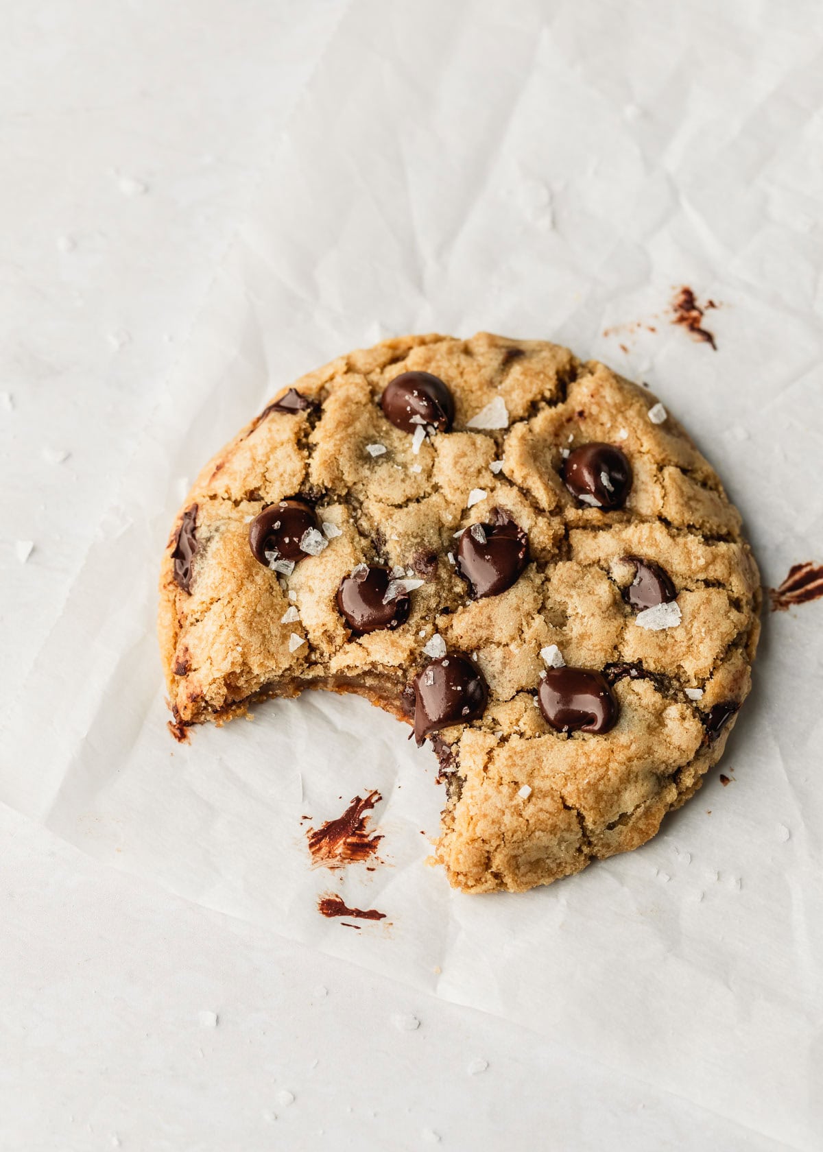 One chocolate chip cookie with a bite taken out of it on parchment paper with a white background.