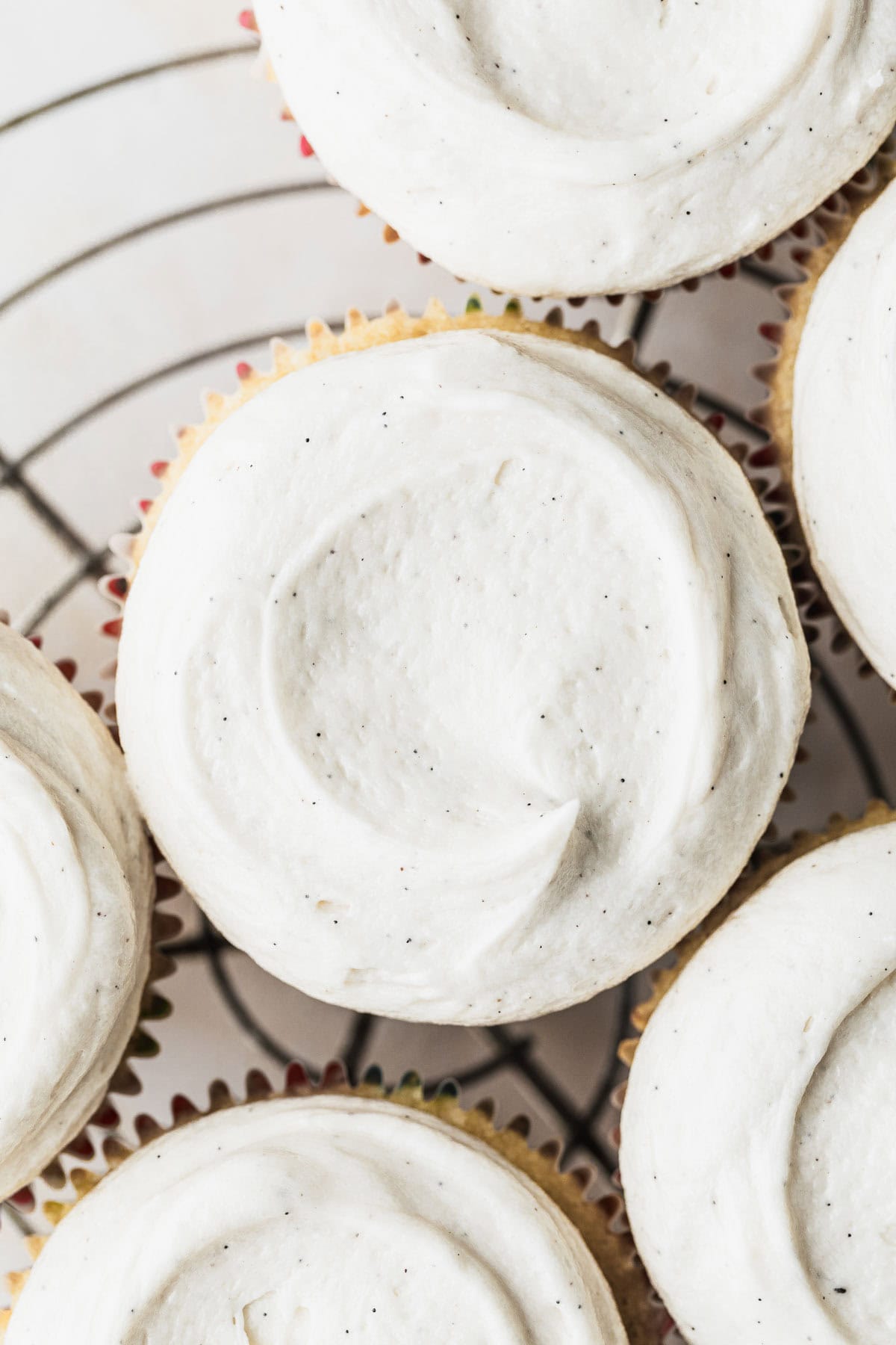 Six cupcakes with small batch vanilla buttercream on a wire rack with a beige background.
