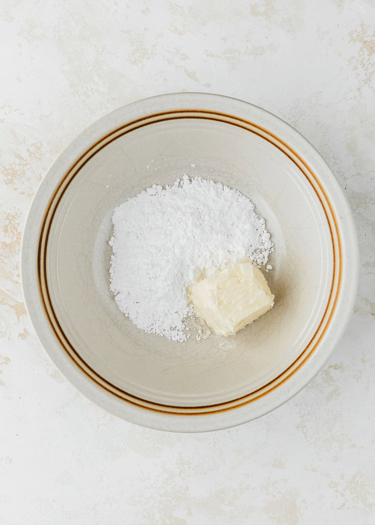 A white bowl of powdered sugar and butter on a tan counter.