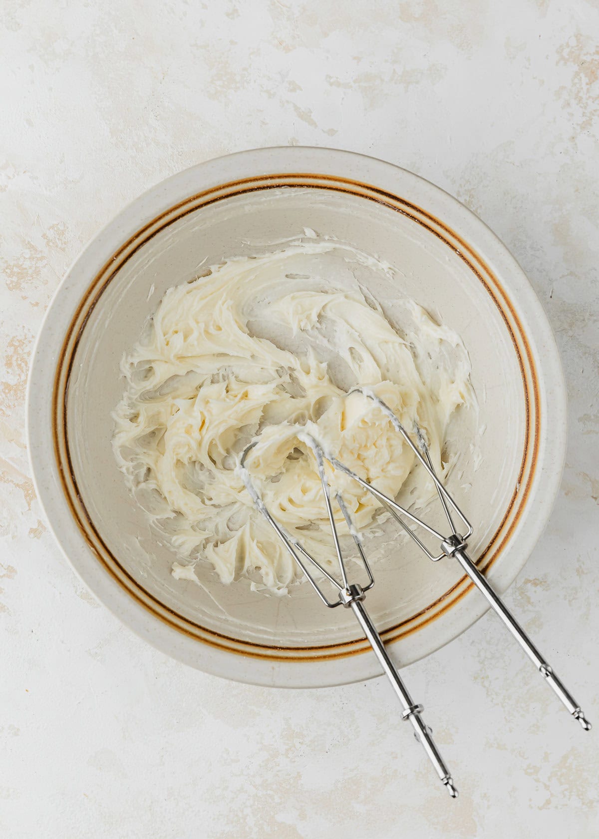 A white bowl of creamed butter and sugar with beaters on a tan table.