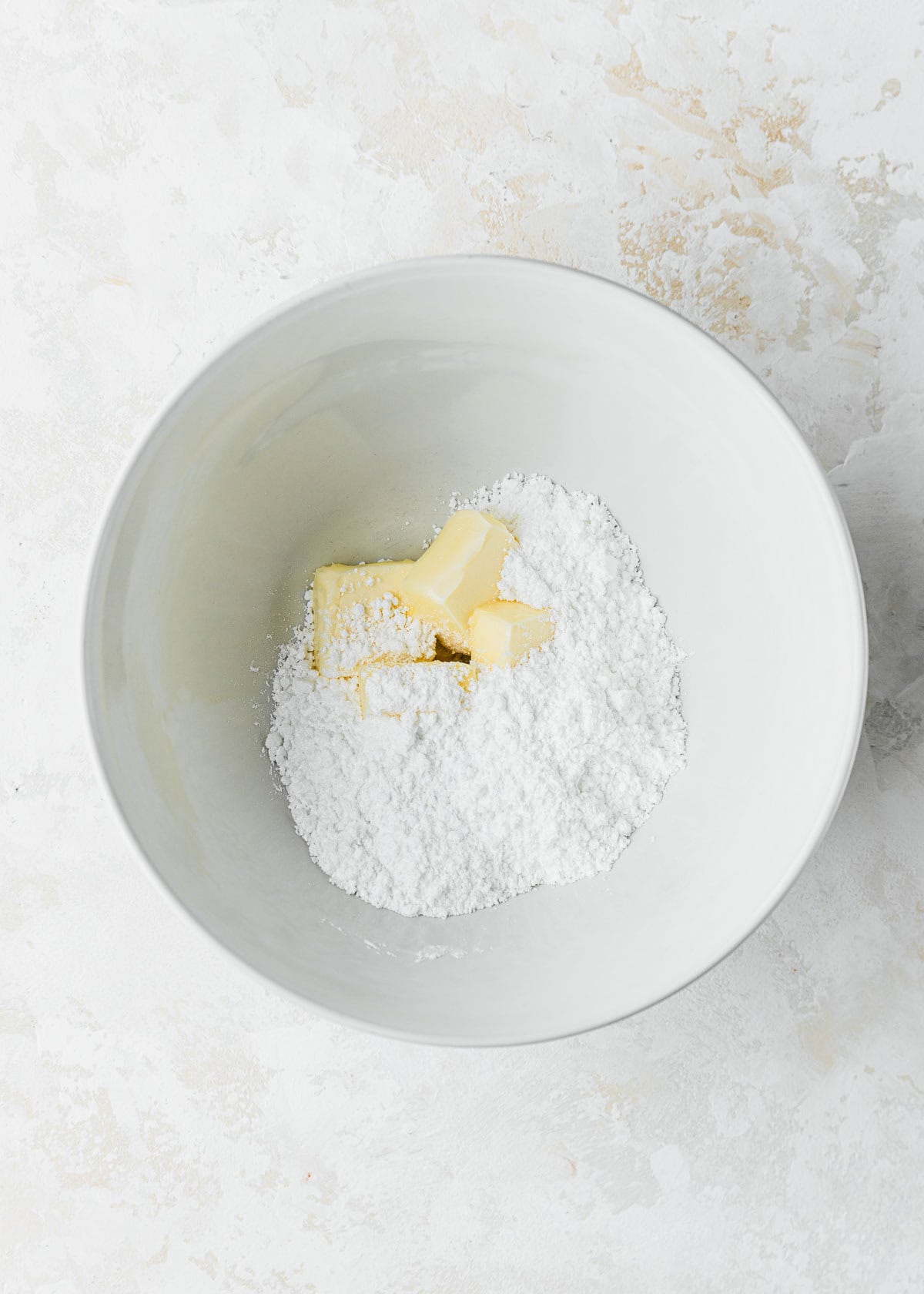 A white bowl of powdered sugar and butter on a beige counter.