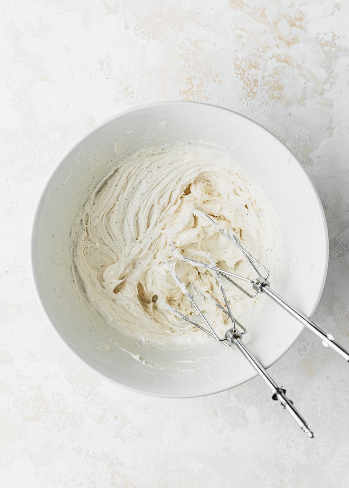 A white bowl of small batch vanilla buttercream and beaters on a beige counter.