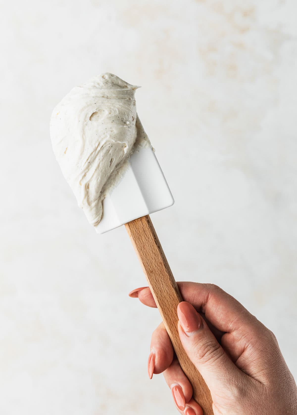 A hand holding a rubber spatula with small batch vanilla buttercream.