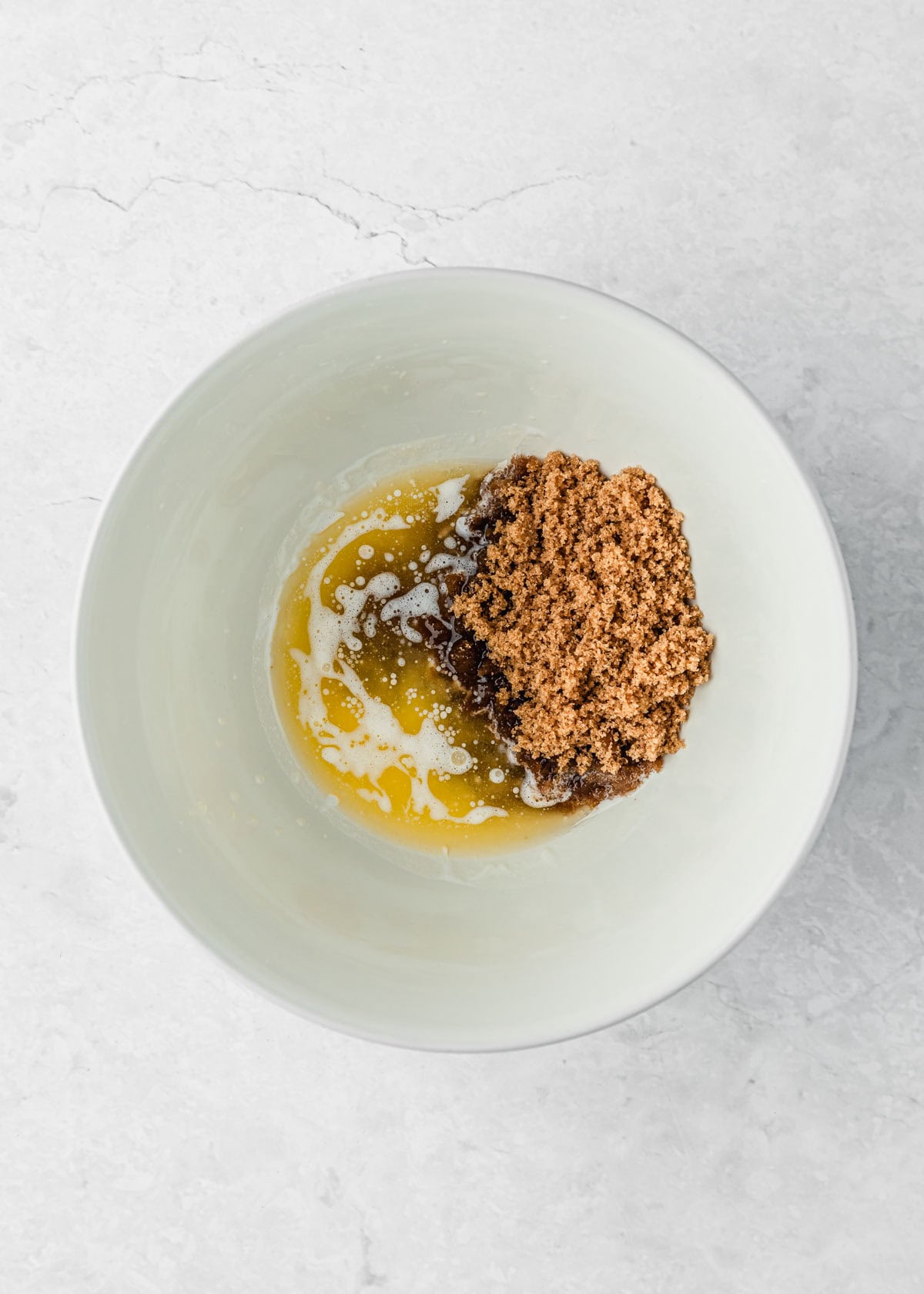 A white bowl of melted butter and brown sugar on a white counter.