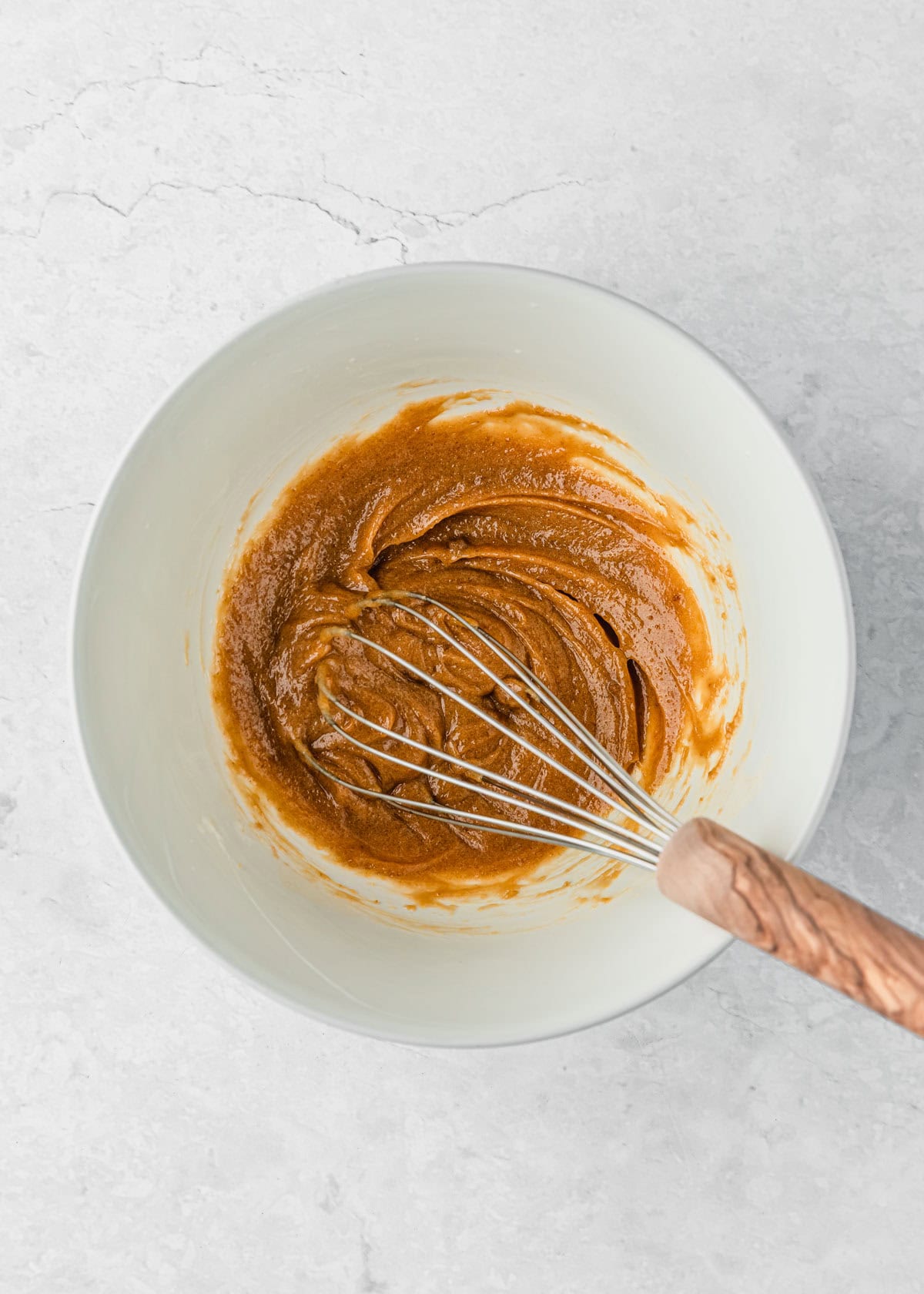 A white bowl of butter, sugar, and an egg yolk mixed together with a whisk for small batch chocolate chip cookie bars.