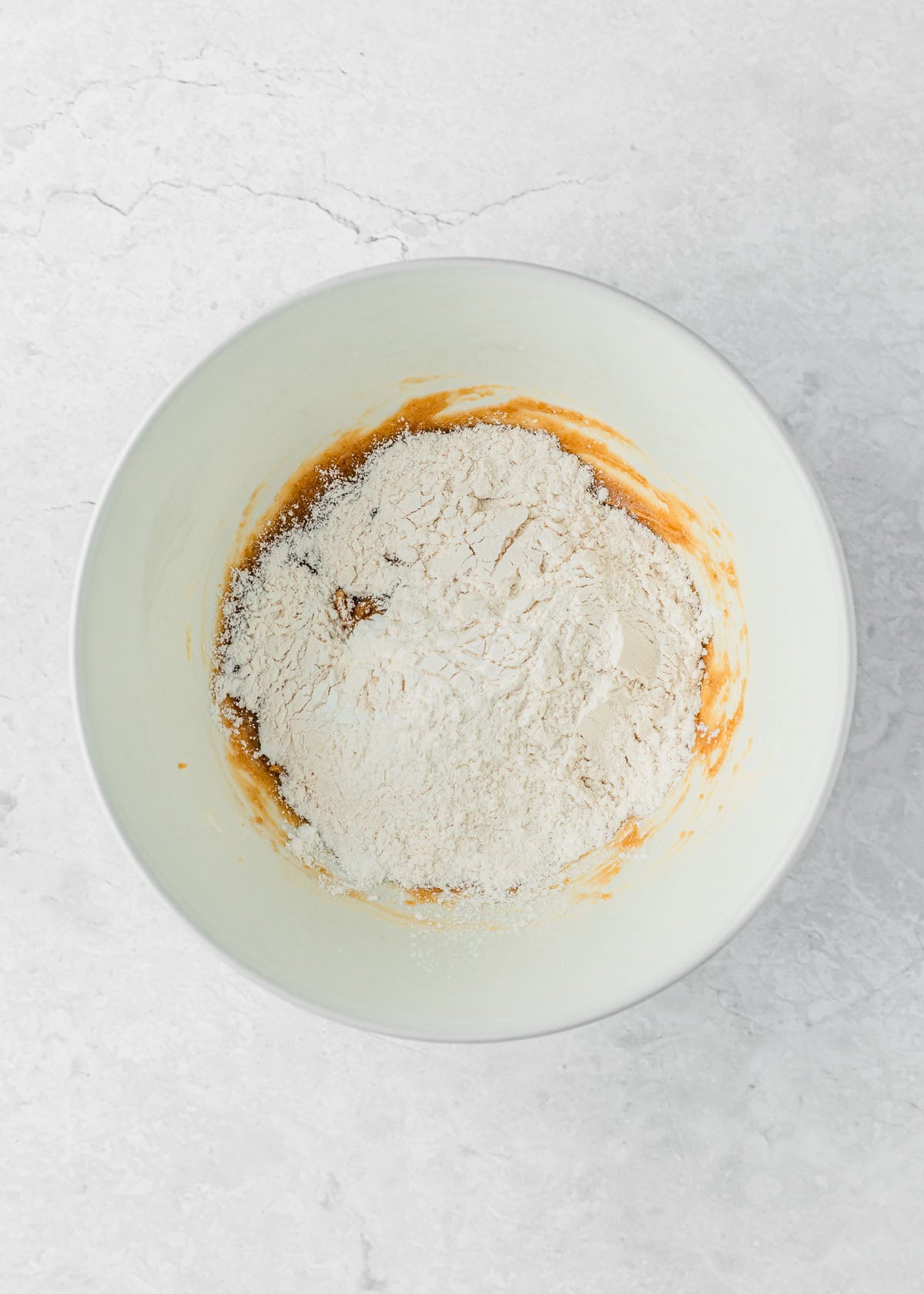 A white bowl of flour, cornstarch, baking powder, and salt on a white counter.