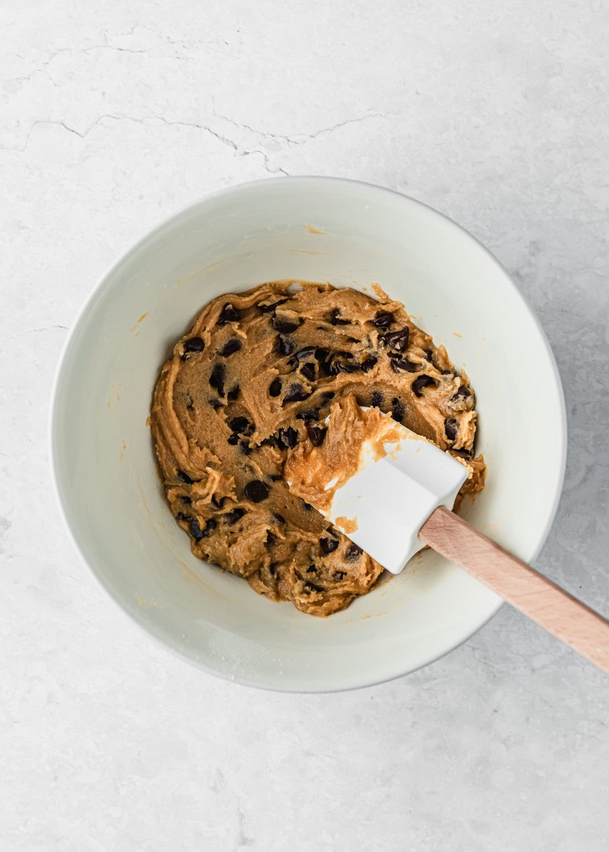 A white bowl of dough for small batch chocolate chip cookie bars on a white marble counter.